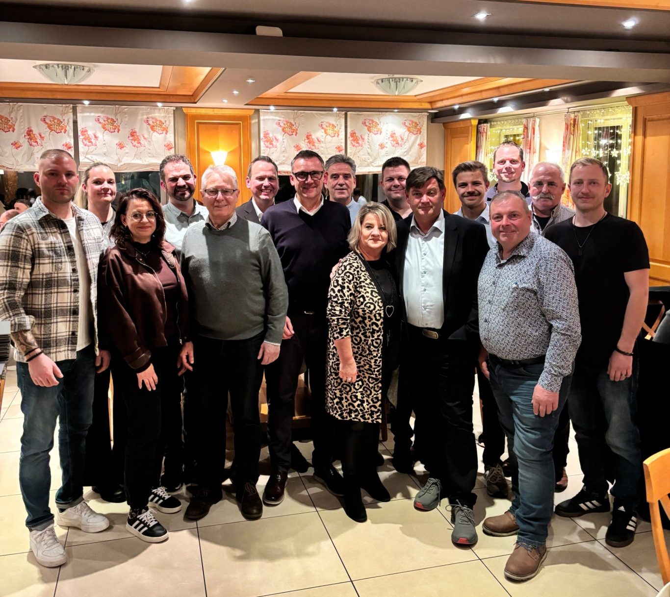 Gruppenszene mit 18 Personen in einem gemütlichen Restaurant, lächelnd und stehend.