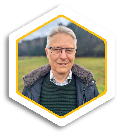 Älterer Mann mit grauen Haaren und Brille, lächelt vor einer grünen Wiese.