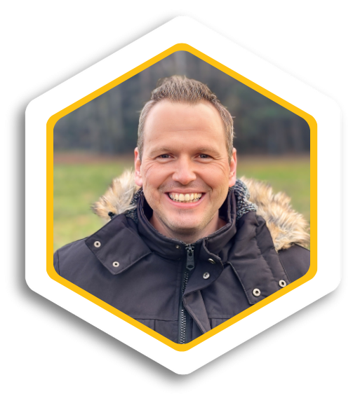 Lächelnder Mann im Freien, trägt eine Jacke mit Fellkragen, unscharfer Hintergrund.