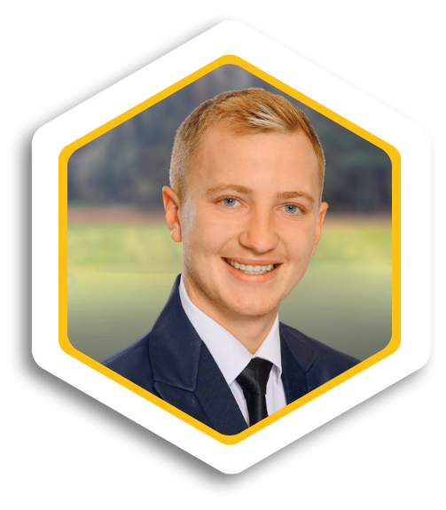 Mann mit blonden Haaren, lächelnd in einem Anzug, mit unscharfem Hintergrund.