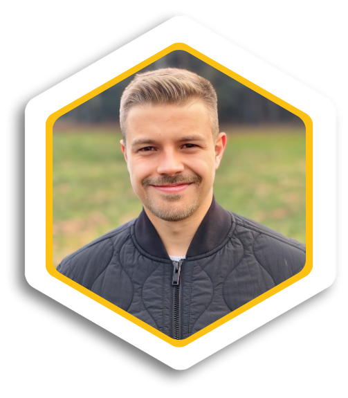 Mann mit kurzem, blonden Haar und schwarzer Jacke, vor verschwommenem grünen Hintergrund.