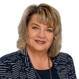 Porträt einer Frau mit blonden, lockigen Haaren und einem professionellen Outfit.