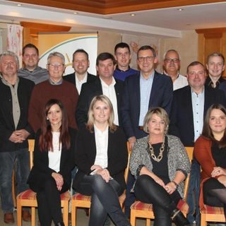 Gruppenzusammenkunft von 15 Personen, sitzend und stehend, in formeller Umgebung.