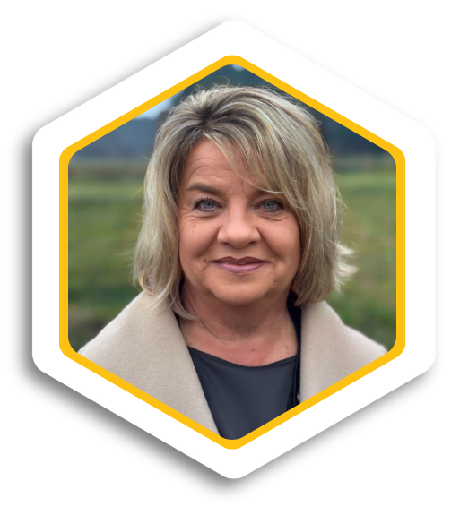 Frau mit blonden Haaren, lächelt vor einer grünen Wiese.