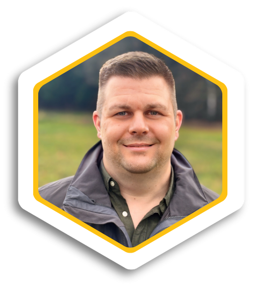 Mann mit kurzem Haar und freundlichem Lächeln, steht auf einer grünen Wiese.